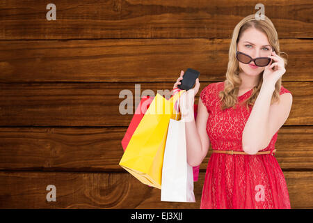 Composite image of cute woman holding shopping bags and her smartphone Stock Photo