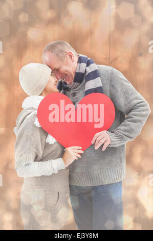 Composite image of happy mature couple in winter clothes holding red heart Stock Photo