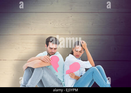 Composite image of sad couple sitting holding two halves of broken heart Stock Photo