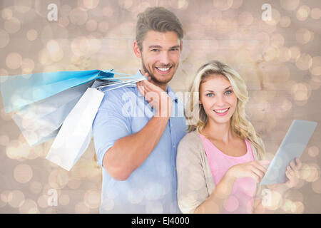 Composite image of attractive young couple holding shopping bags using tablet pc Stock Photo