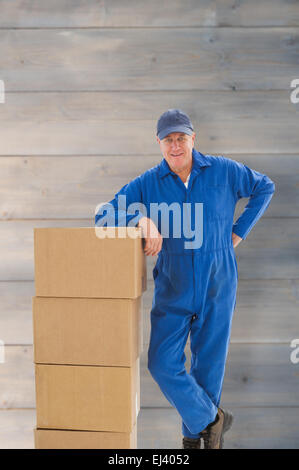 Composite image of happy delivery man leaning on pile of cardboard boxes Stock Photo