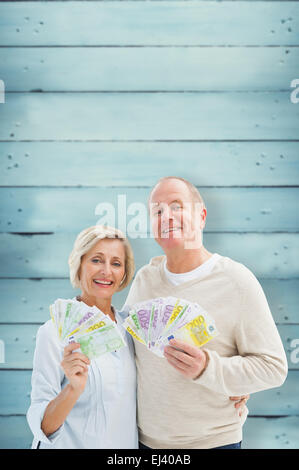 Composite image of happy mature couple smiling at camera showing money Stock Photo