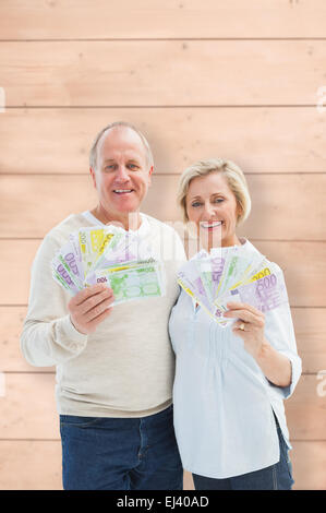 Composite image of happy mature couple smiling at camera showing money Stock Photo