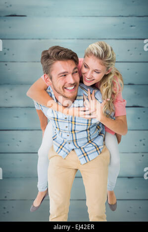 Composite image of handsome man giving piggy back to his girlfriend Stock Photo