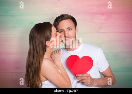 Composite image of woman kissing man as he holds heart Stock Photo