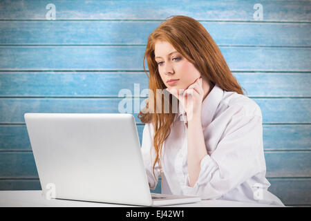 Composite image of pretty redhead working on laptop Stock Photo