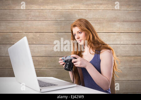 Composite image of pretty redhead working on laptop and camera Stock Photo
