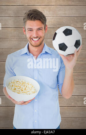 Composite image of handsome young man holding ball and popcorn Stock Photo