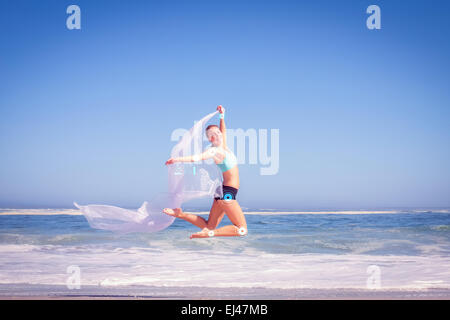 Composite image of fit woman jumping gracefully on the beach with scarf Stock Photo