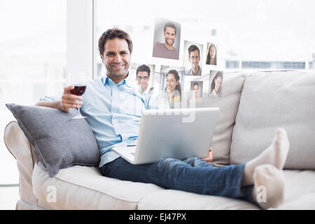 Composite image of smiling handsome man relaxing on sofa with glass of red wine using laptop Stock Photo