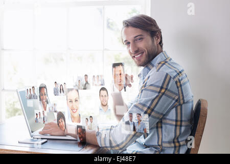 Composite image of handsome man sitting at table using laptop Stock Photo