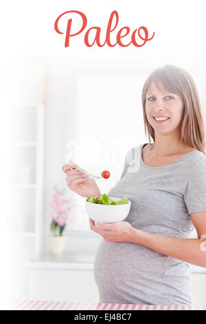 Paleo against charming pregnant woman eating a cherry tomato while standing Stock Photo