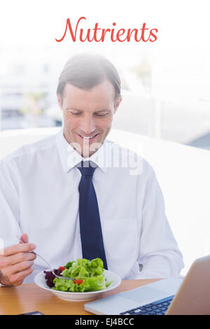 Nutrients against smiling businessman eating a salad on his desk Stock Photo