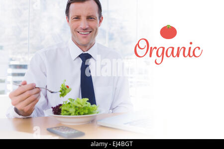 Organic against happy businessman eating a salad on his desk Stock Photo