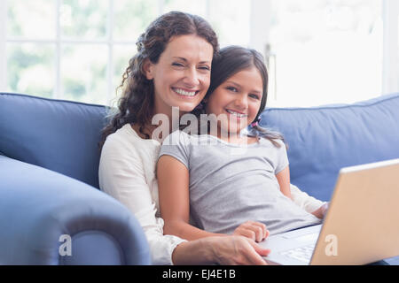Happy mother and daughter sitting on the couch and using laptop Stock Photo