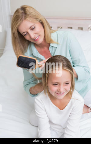 Smiling mother brushing her daughters hair Stock Photo