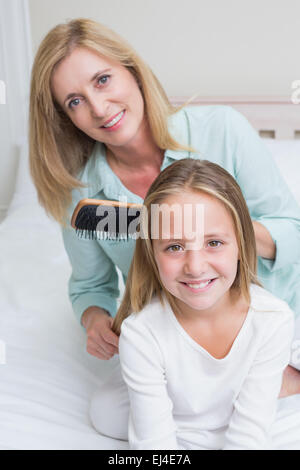 Smiling mother brushing her daughters hair Stock Photo