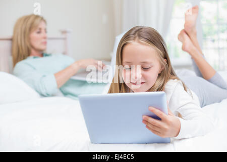 Mother using laptop while daughter using tablet pc on the bed