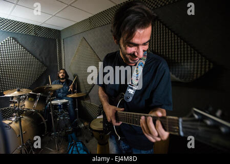 Rap-singer and musician Payman plays on drums and young filmmaker Moien plays on guitar during their rehearsal in sound recording part of young Iranian artists' studio, Tehran, Iran Stock Photo