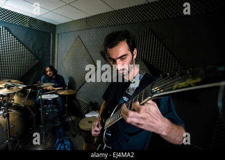Rap-singer and musician Payman plays on drums and young filmmaker Moien plays on guitar during their rehearsal in sound recording part of young Iranian artists' studio, Tehran, Iran Stock Photo