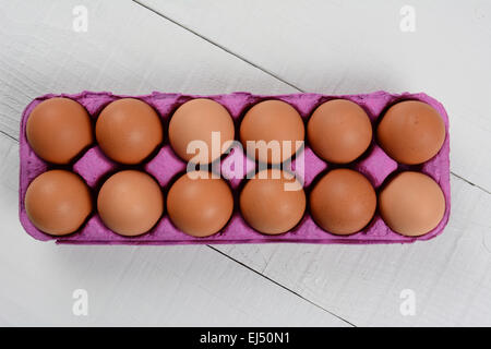 High angle shot of a dozen organic brown eggs in a pink cardboard carton on a rustic white wood table. Horizontal format with co Stock Photo