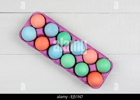 A pink one dozen carton of dyed Easter Eggs on a white wood kitchen table. Horizontal format with the carton at an angle. Stock Photo