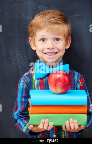 Smiling encoureged ginger boy holding a pile of books Stock Photo