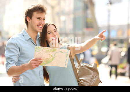 Couple of tourists consulting a city guide searching locations in the street and pointing Stock Photo