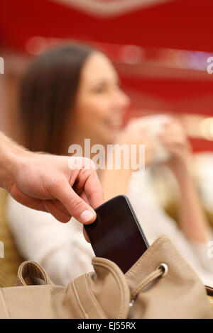 Thief hand stealing a mobile phone from a woman bag while she is relaxed Stock Photo