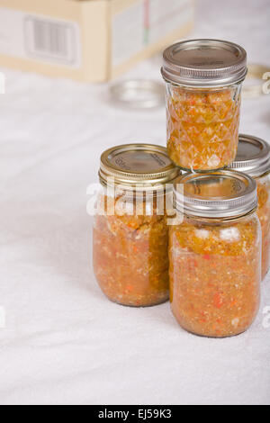 Jars of home-canned relish on a white towel with a canning jar box in the background, prior to par-boiling Stock Photo