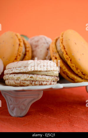 Caramel and vanilla macaroons in vintage bowl on orange and dark wood table setting. Stock Photo