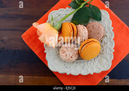 Caramel and vanilla macaroons in vintage bowl on orange and dark wood table setting. Stock Photo