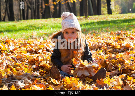 little girl sits on fallen leaves in autumn park Stock Photo