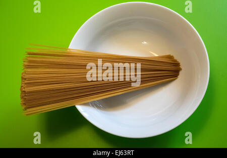 Uncooked whole wheat spaghetti in a white bowl on a green table, pasta Stock Photo