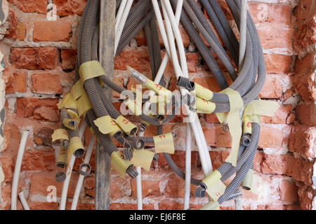 Entwined tangled electrical conduits on the brick wall during renovation works. Stock Photo
