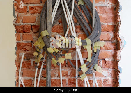 Entwined tangled electrical conduits on the brick wall during renovation works. Stock Photo