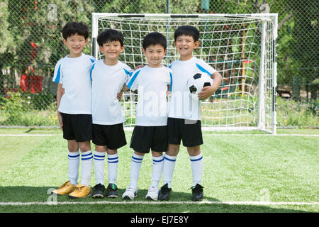 Four boys hug shoulders stood on the football field Stock Photo