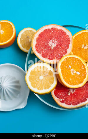 Citruses in a glass bowl on the blue background with a squeezer Stock Photo