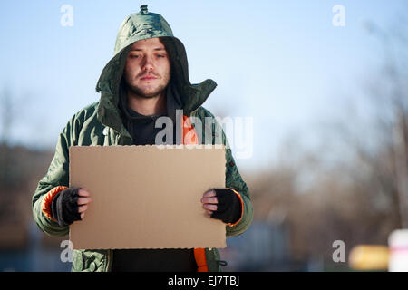 Homeless person with blanck cardboard. Focused on cardboard Stock Photo