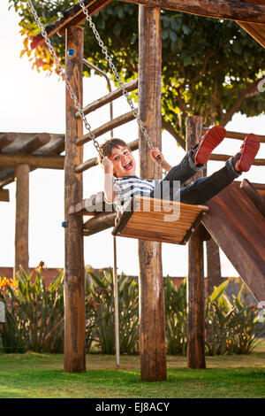 Cute boy playing on swing, having fun. Sunset in the park. Stock Photo
