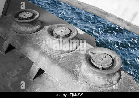 Old grungy rollers for mooring ropes, industrial ship monochrome fragment with blue sea water Stock Photo