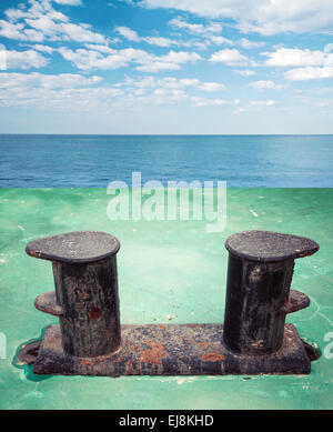 Old black rusted bollard mounted on green ship deck, with sea landscape on a background Stock Photo