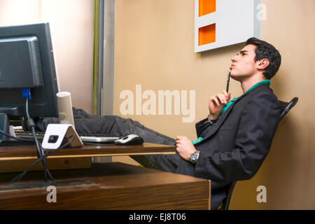 Serious young businessman sitting at desk in office, concentrated and thinking how to solve a problem Stock Photo