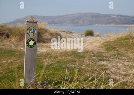 Wooden waymarker / post on the Wales Coastal Path on sand dunes / beach at Conwy, North Wales with view of Llandudno and sea Stock Photo