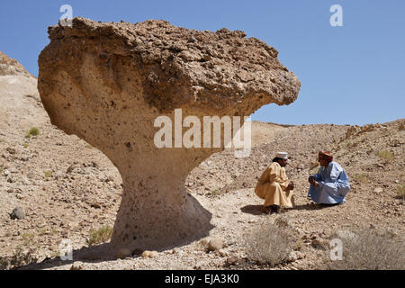 Omani men talking beneath desert mushroom near Mazara, Oman Stock Photo