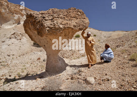 Omani men beneath desert mushroom near Mazara, Oman Stock Photo