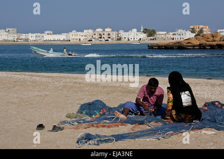 Fisherman and woman mending nets on beach, Sur, Oman Stock Photo