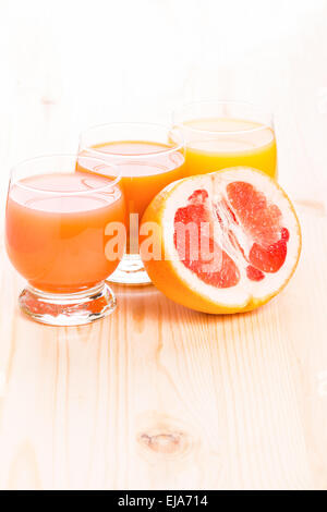 Three glasses of juice with cut in half grapefruit on wooden table. Healthy food background Stock Photo