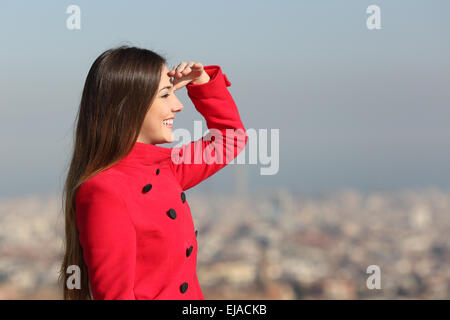 Woman looking forward in winter with a red coat with city in the background Stock Photo