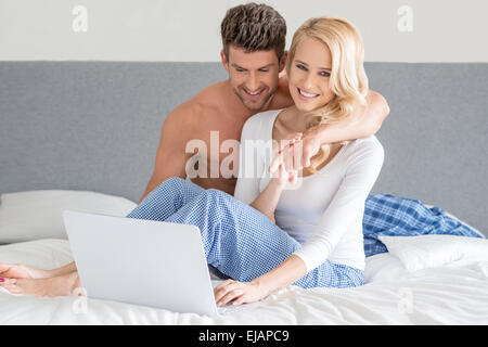 Young couple relaxing in bed using a laptop Stock Photo
